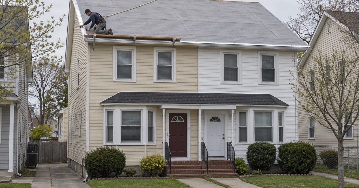 A roofer fitting drip edge along the rake of a side-by-side duplex being re-roofed in Lakewood.
